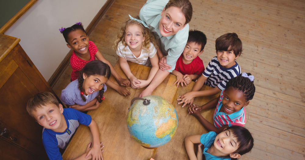 Cute pupils smiling around a globe in classroom with teacher at the elementary school-2